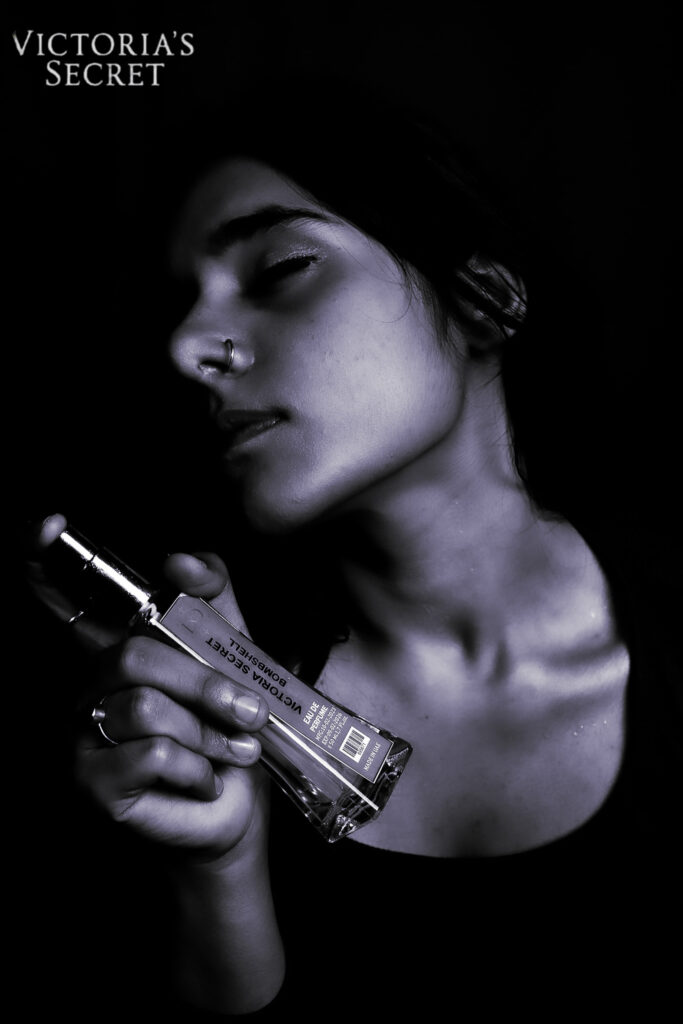 A product photography for Victoria's secret, where a model is holding the perfume bottle and enjoying the essence of the perfume.